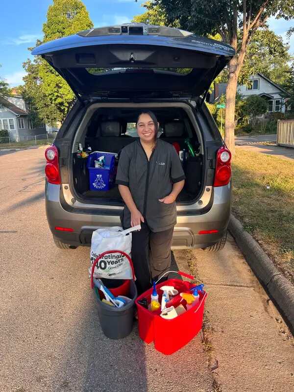 Diana in casual clothes holding cleaning supplies, standing in a tidy home with bright natural light, conveying a friendly and welcoming atmosphere